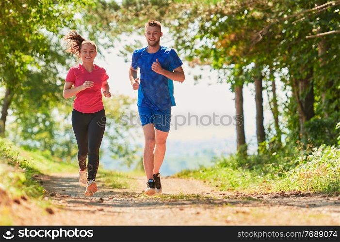young happy couple enjoying in a healthy lifestyle while jogging on a country road through the beautiful sunny forest, exercise and fitness concept
