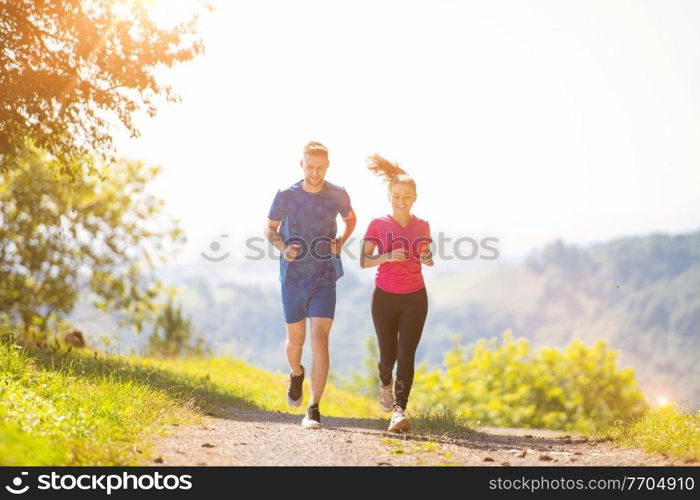 young happy couple enjoying in a healthy lifestyle while jogging on a country road through the beautiful sunny forest, exercise and fitness concept