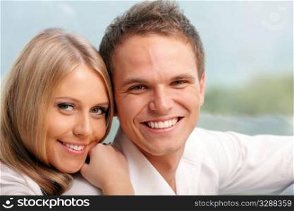 Young happy couple hugging at home with a beautiful seaview behind their window
