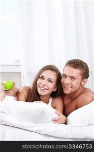 Young happy couple in bed with apple