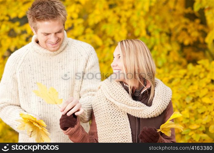 Young happy couple in love holding leaves in autumn park