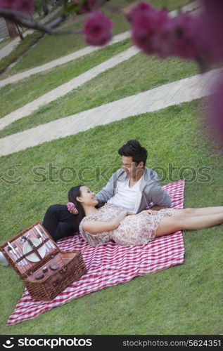 Young happy couple lying on a blanket together while having a picnic in the park, blossoms in the foreground