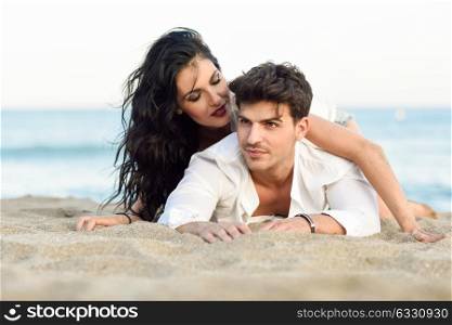 Young happy couple lying on the sand in a beautiful beach. Funny Man and woman wearing casual clothes.