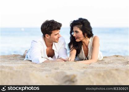 Young happy couple lying on the sand in a beautiful beach. Lovers wearing casual clothes.