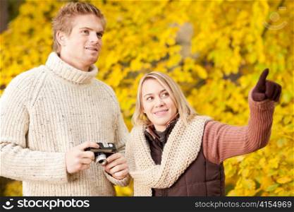 Young happy couple making photo in autumn park pointing at