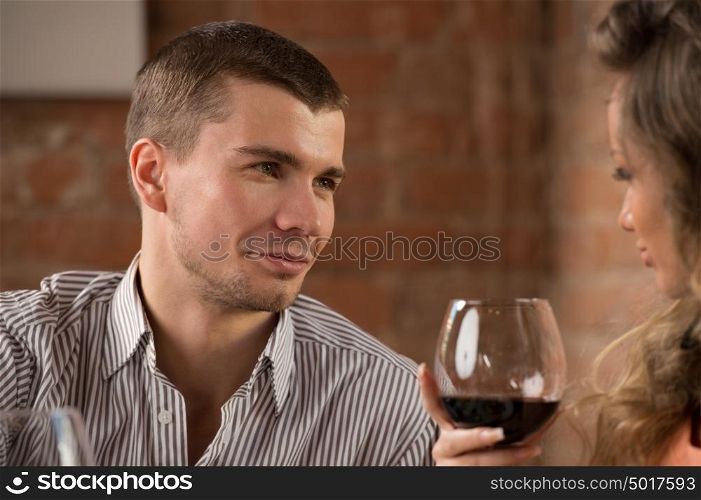 Young happy couple on romantic date drinking glass of red wine at restaurant, celebrating valentine day