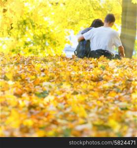 Young happy couple sitting in the autumn park with yellow trees
