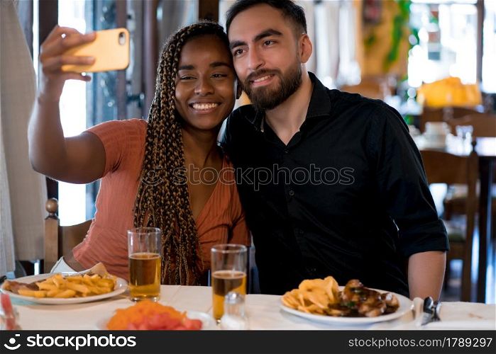 Young happy couple taking a selfie with a mobile phone while enjoying a date at a restaurant.