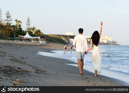 Young happy couple walking in a beautiful beach. Funny Man and woman wearing casual clothes. Rear view.