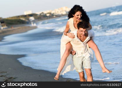 Young happy couple walking in a beautiful beach. Funny Man and woman wearing casual clothes. Male carrying his girlfriend in his arms.