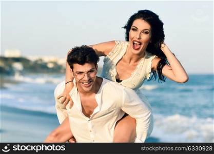 Young happy couple walking in a beautiful beach. Funny Man and woman wearing casual clothes. Male carrying his girlfriend in his arms.