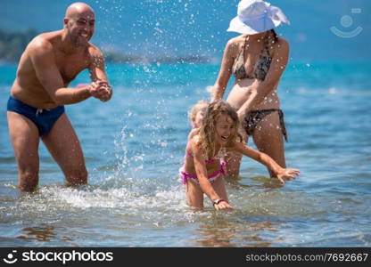 young happy couple with cute little daughters having fun while splashing each other in the shallow water of the sea during Summer vacation  Healthy family holiday concept