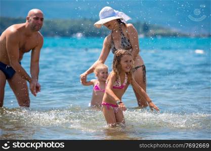 young happy couple with cute little daughters having fun while splashing each other in the shallow water of the sea during Summer vacation  Healthy family holiday concept