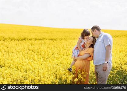 young happy family among the yellow flowering field. Family rest. Pregnant mother, the father and the little daughter have a rest among yellow colza. young happy family among the yellow flowering field. Family rest. Pregnant mother, the father and the little daughter have a rest among yellow colza.