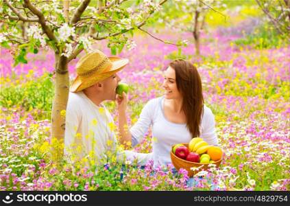 Young happy family having fun in spring blooming garden, cute woman feeding her boyfriend apple, romance and love concept