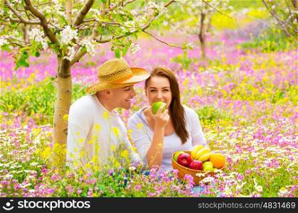 Young happy family having picnic on floral field in spring garden, eating healthy organic food, holiday and vacation concept