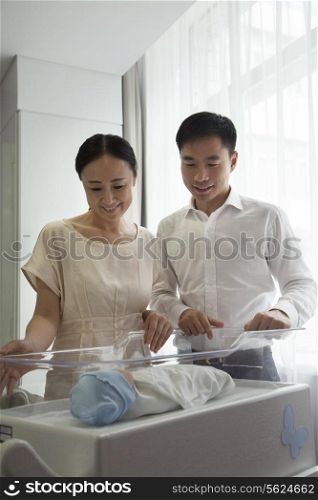 Young happy family looking down at their newborn in the hospital nursery