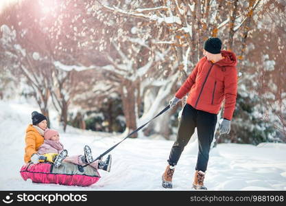 Young happy family of dad and kids sledding and having fun outdoors in winter. Family of dad and kids vacation on Christmas eve outdoors