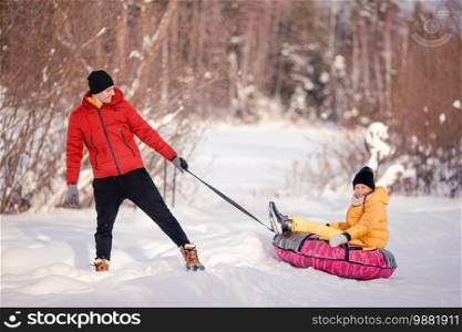 Young happy family of father and kid sledding and having fun outdoors in winter. Family of dad and kids vacation on Christmas eve outdoors