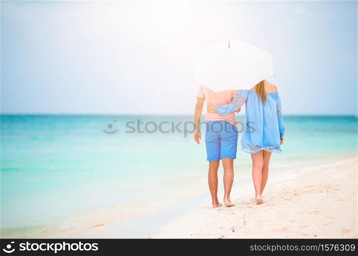 Young happy family on the beach with umbrella to hide from sun. Young family of two on white beach have a lot of fun