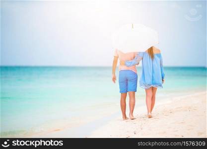 Young happy family on the beach with umbrella to hide from sun. Young family of two on white beach have a lot of fun