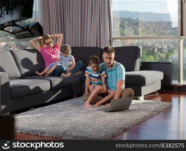 young happy family relaxing at home using laptop and tablet computers in luxury living room