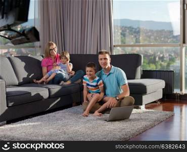 young happy family relaxing at home using laptop and tablet computers in luxury living room
