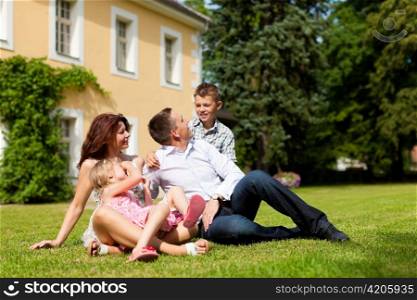 Young happy family sitting in the sun on the lawn in front of their new home - a villa