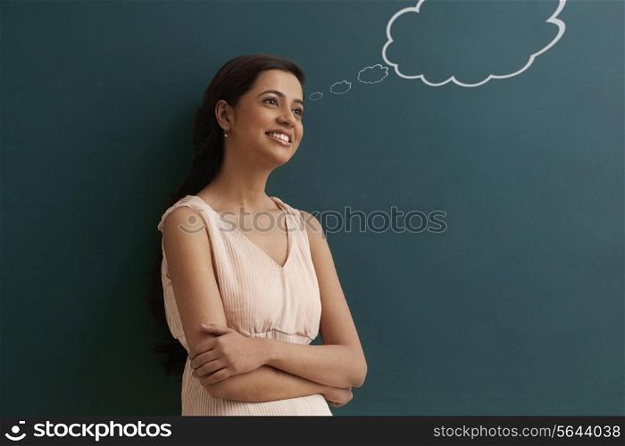 Young happy female teacher with thought bubble on chalk board