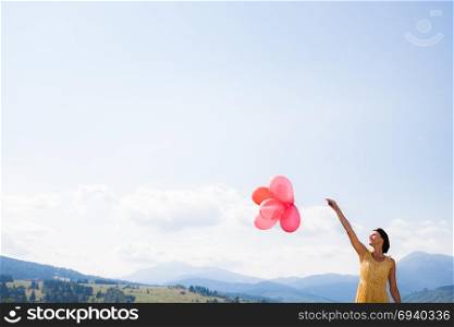 Young happy girl holding red balloons over blue sky