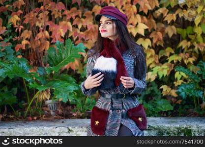 Young happy girl with very long hair smiling and wearing winter coat and cap in autumn leaves background. Lifestyle and fashion concept.. Young girl with very long hair smiling and wearing winter coat and cap in autumn leaves background.