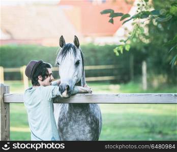 Young happy guy laughs and hugs his horse at summer outdoor nature