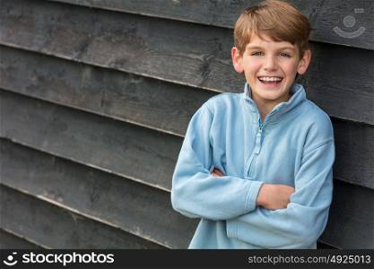 Young happy laughing male boy blond child outside leaning against a wall outside arms folded and laughing
