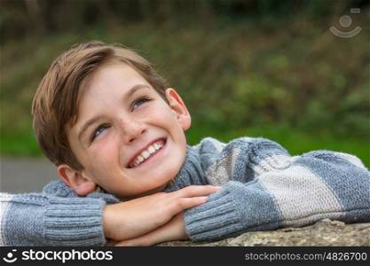 Young happy laughing male boy blond child outside leaning on his hands and looking up in autumn fall sunshine