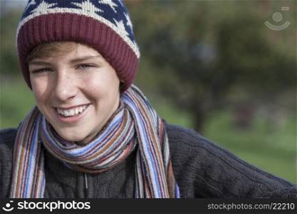 Young happy laughing male boy teenager blond child outside in in warm clothing woolen hat and scarf