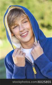 Young happy laughing male boy teenager blond child outside in summer sunshine wearing a blue hoody