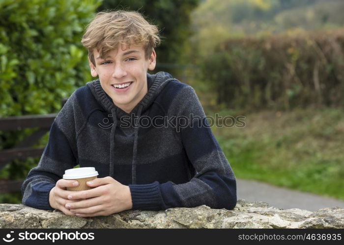 Young happy laughing male boy teenager blond child young adult drinking takeaway coffee outside in fall sunshine