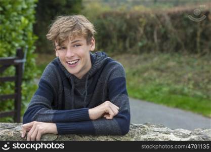 Young happy laughing smiling teenager male boy blond child outside leaning on a wall in autumn fall sunshine