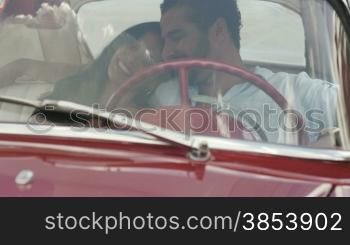 Young happy man and woman dating in red convertible vintage car from the 1950s