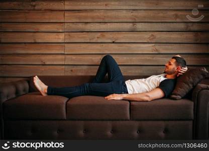 Young happy man lying on couch, side view. Relaxation on sofa. Male person relax