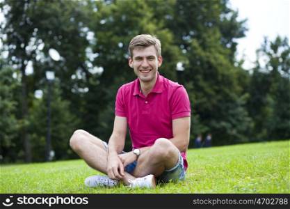 Young happy man sitting on the lawn in the summer park