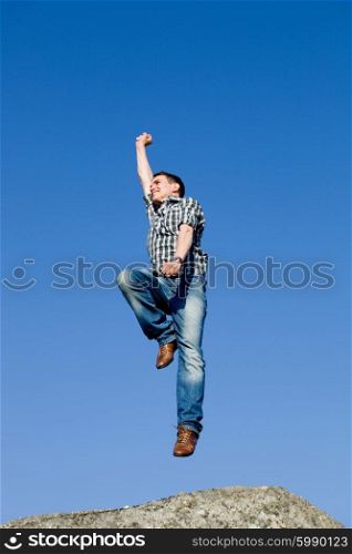 young happy man, with a big jump, on top of a rock