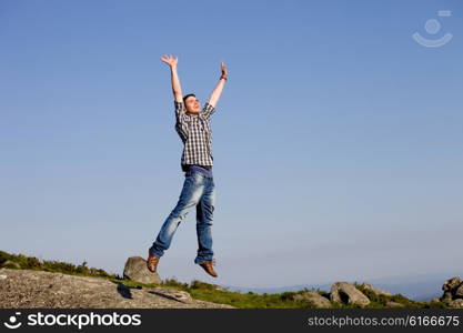 young happy man, with a big jump, on top of a rock