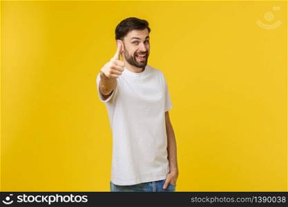 Young happy man with thumbs up sign in casuals isolated on yellow background.. Young happy man with thumbs up sign in casuals isolated on yellow background