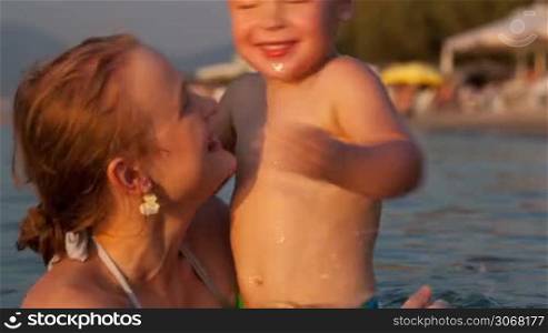 Young happy mother toss up her little three year old sonny while swimming in the sea near the beach smiling and laughing while jumping