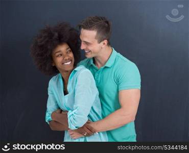 Young happy multiethnic couple laughing and hugging in front of gray chalkboard