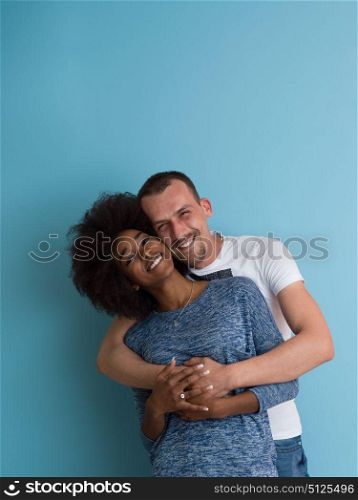 Young happy multiethnic couple laughing and hugging isolated on a blue background