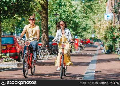 Young happy ouple on bikes in old streets in Amsterdam. Young happy caucasian couple on bikes in old streets in Amsterdam