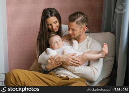Young happy parents hold their baby son in their arms and smile looking at him