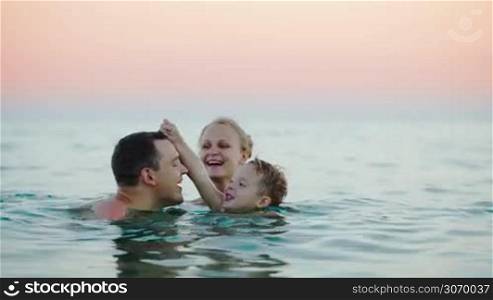 Young happy parents with son bathing in sea. Boy playing with dad and kissing him